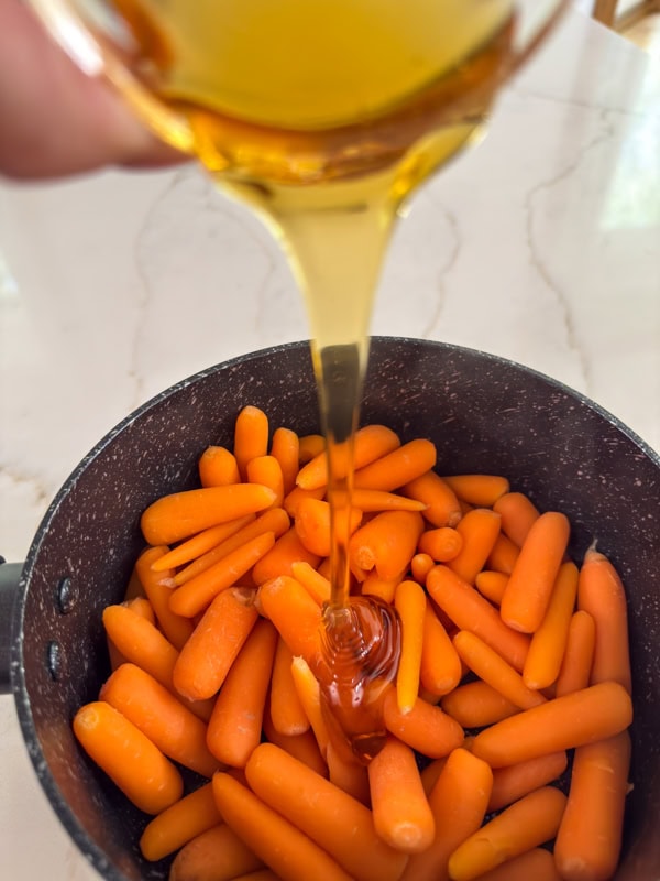 The cooked carrots in the pan with honey being poured down over them.