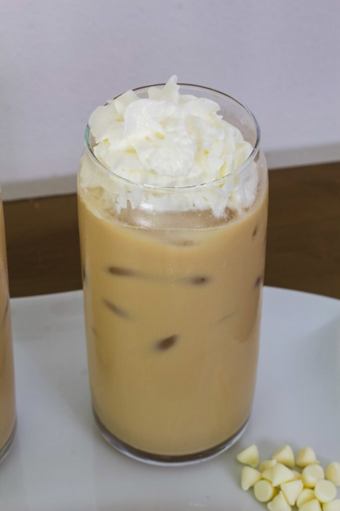 Overhead shot of one Iced White Chocolate Mocha in a glass with white chocolate chips next to it.