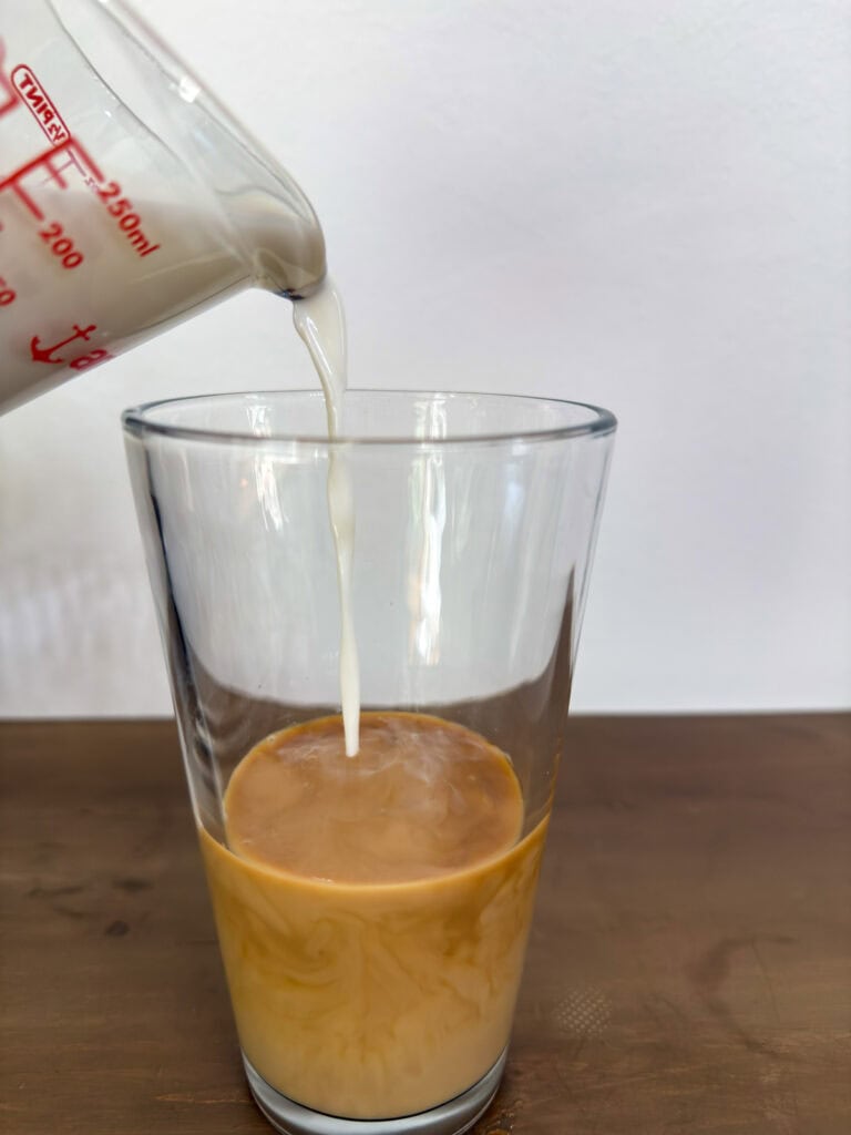 Milk being poured into a glass with homemade cold brew coffee in it.