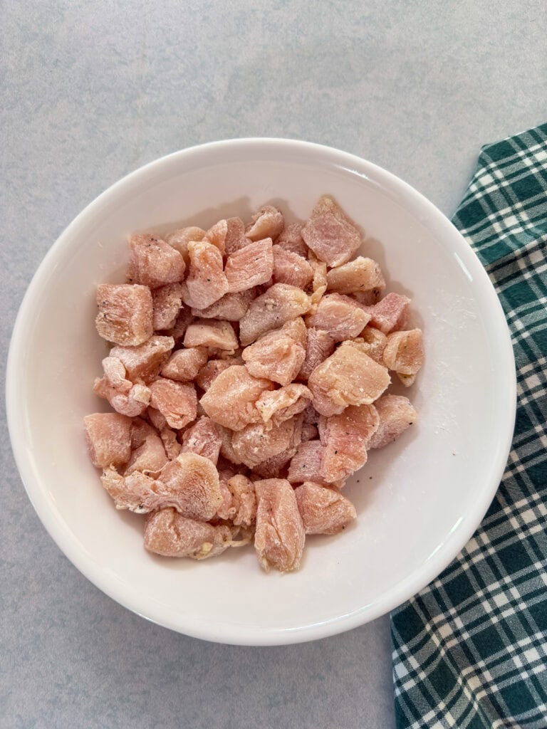 The cut up chicken chunks tossed in corn starch in a white bowl.