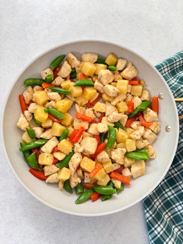 The cooked chicken with the pineapple chunks, red bell pepper and sugar snap peas added in the skillet.
