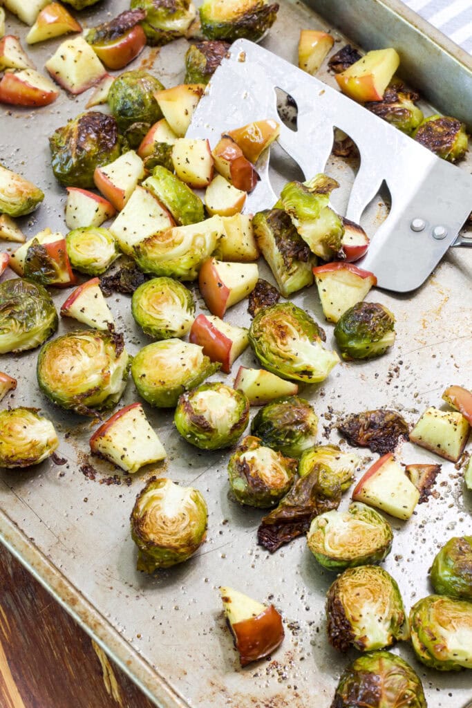 The Oven Roasted Brussels Sprouts with Apples on a rimmed baking sheet with a metal turner on it.