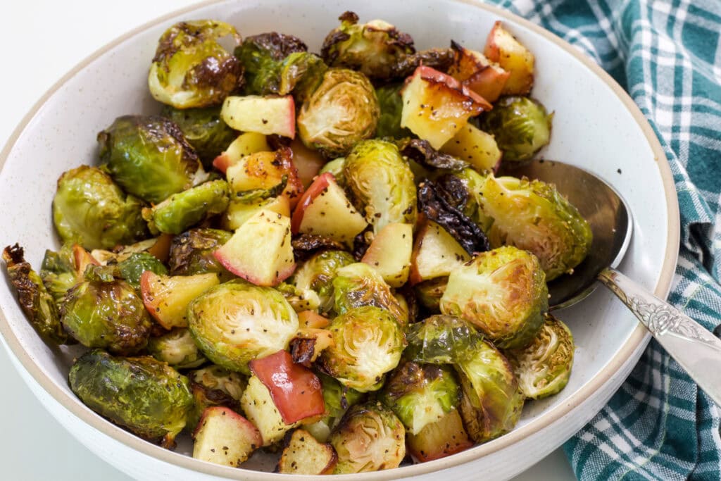 The finished Brussels sprouts in a serving dish with a spoon in it also.