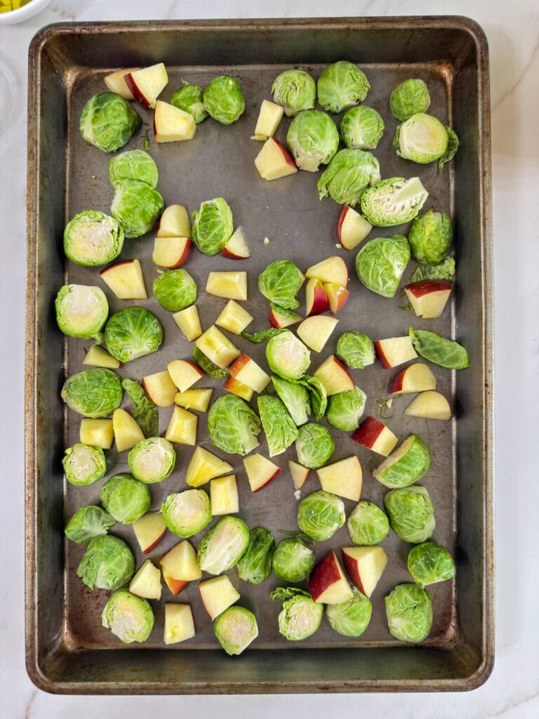 The chopped apple and halved Brussels sprouts on a rimmed baking sheet.