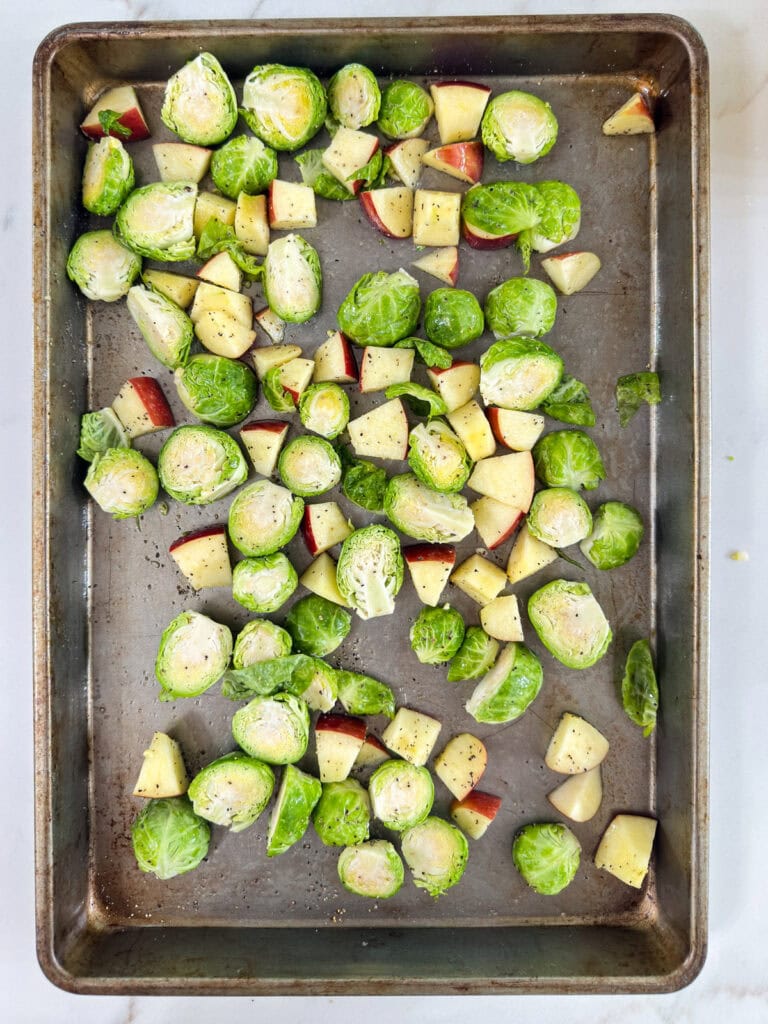 The cut Brussels sprouts and apples on the baking sheet after they've been drizzled with olive oil and seasoned with salt and pepper.