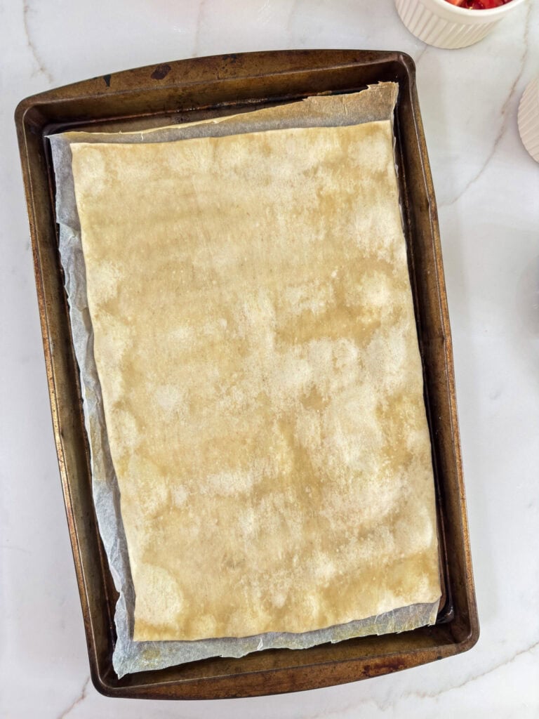 The par-baked pizza crust on a large baking sheet.