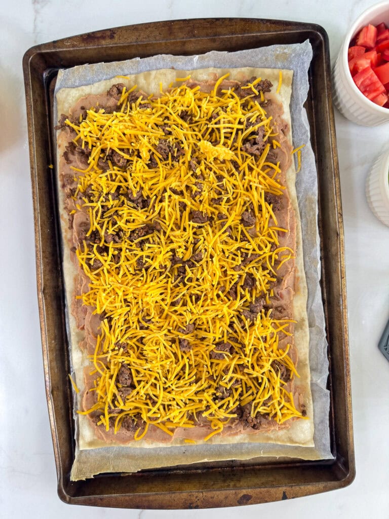 The pizza crust topped with the cooked ground beef, beans and cheese before being baked.