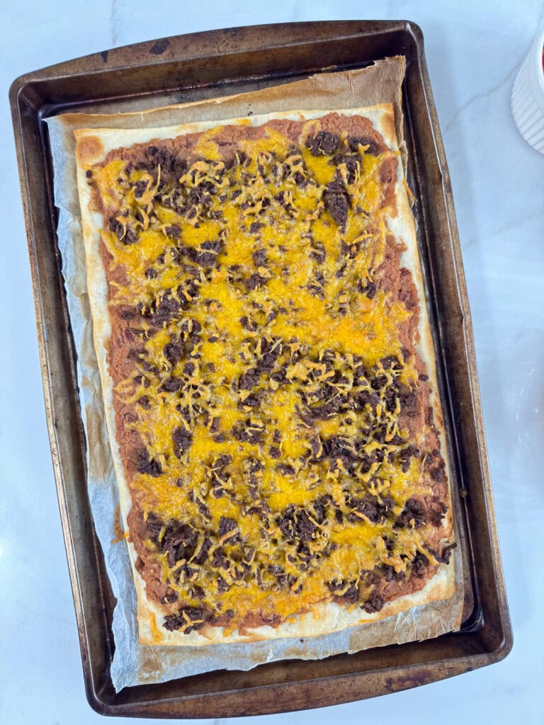 The pizza crust topped with beef, beans and cheese after coming out of the oven.
