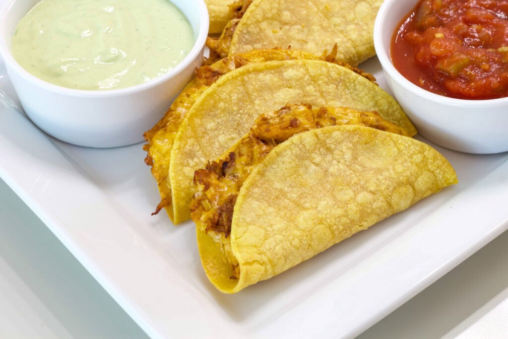 Close up pf several tacos on a plate with sauces to dip them in.