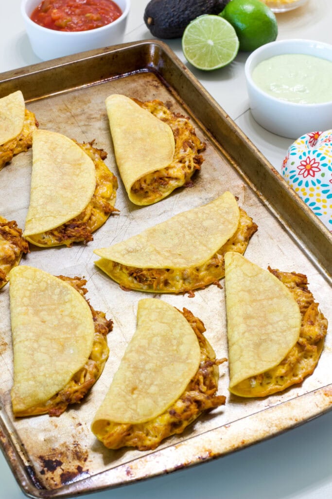 Eight Baked Chicken Tacos on a rimmed baking sheet after they came out of the oven.