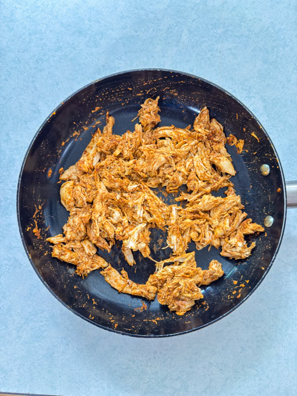 The shredded chicken and taco seasoning in a skillet after being warmed up.