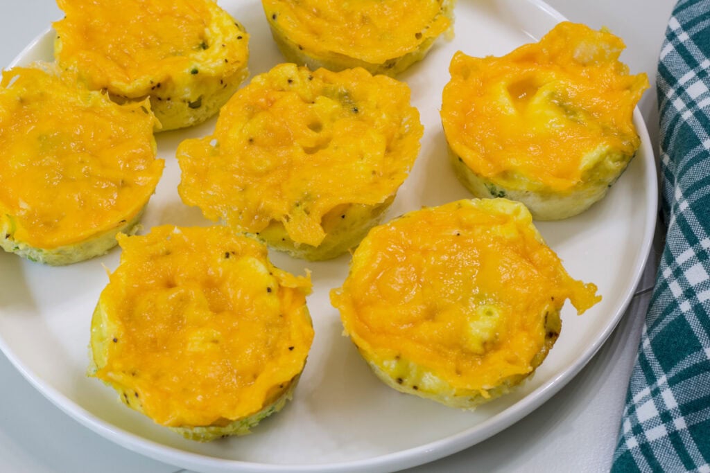 Seven baked Broccoli Cheddar Egg Bites on a white plate.