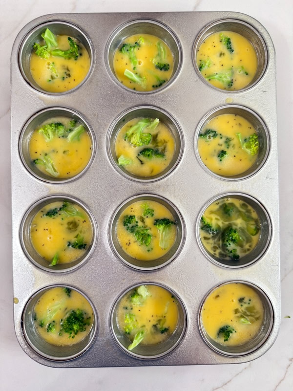 The egg mixture and broccoli in a muffin tin ready for the cheese to be added.