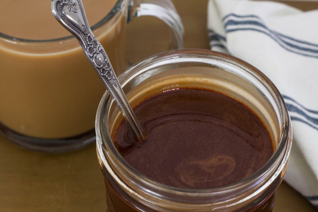 A jar of homemade chocolate syrup and a cup of coffee sitting next to it.