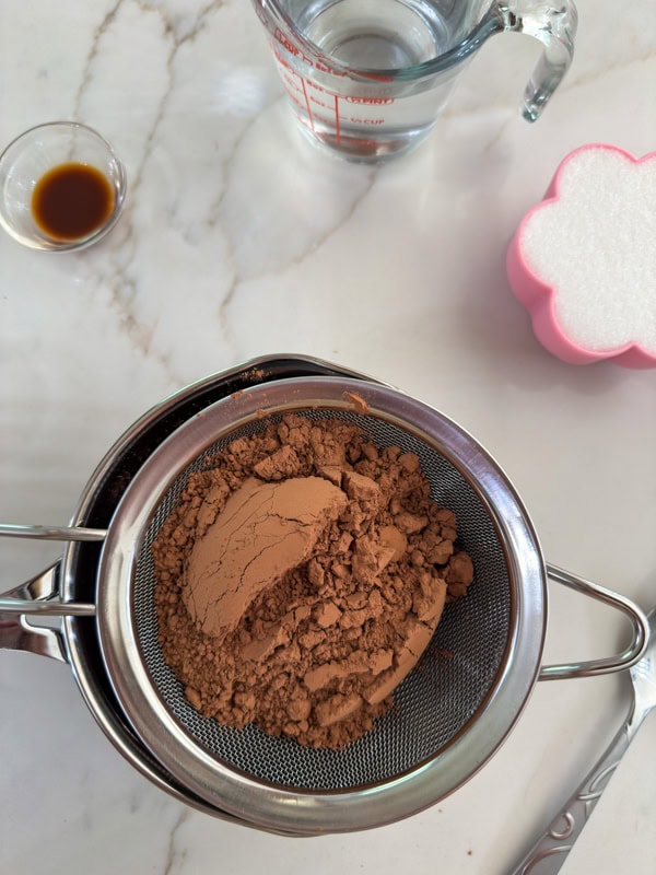The unsweetened cocoa powder in a mesh strainer over a small saucepan.