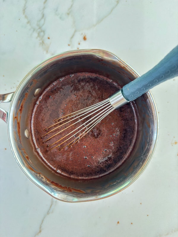 The finished chocolate coffee syrup in a saucepan with a whisk in it.