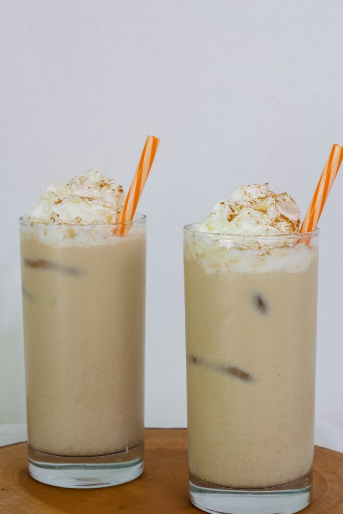 Two finished Iced Pumpkin Spice Lattes on a wooden board.