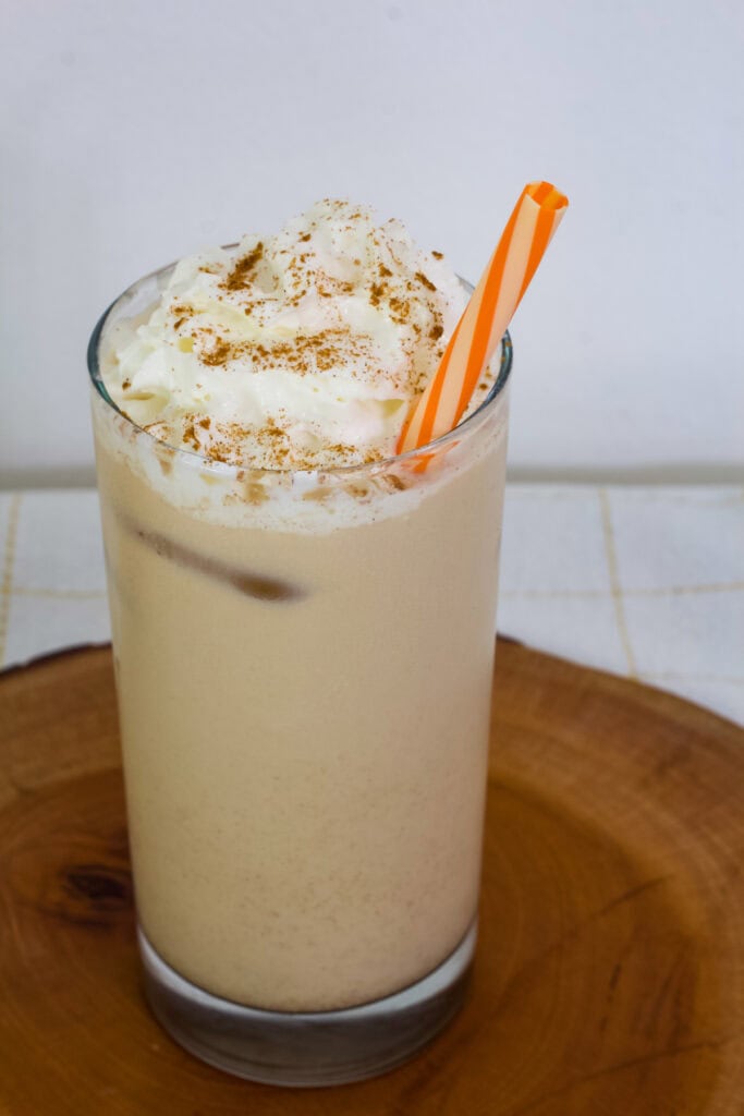 Overhead view of one glass of Iced Pumpkin Spice Latte with an orange striped straw in it.
