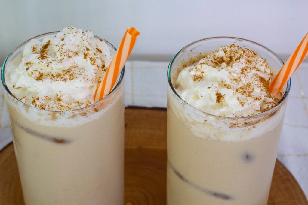 Overhead shot of two glasses of Iced Pumpkin Spice Latte topped with whipped topping and a dusting of cinnamon.