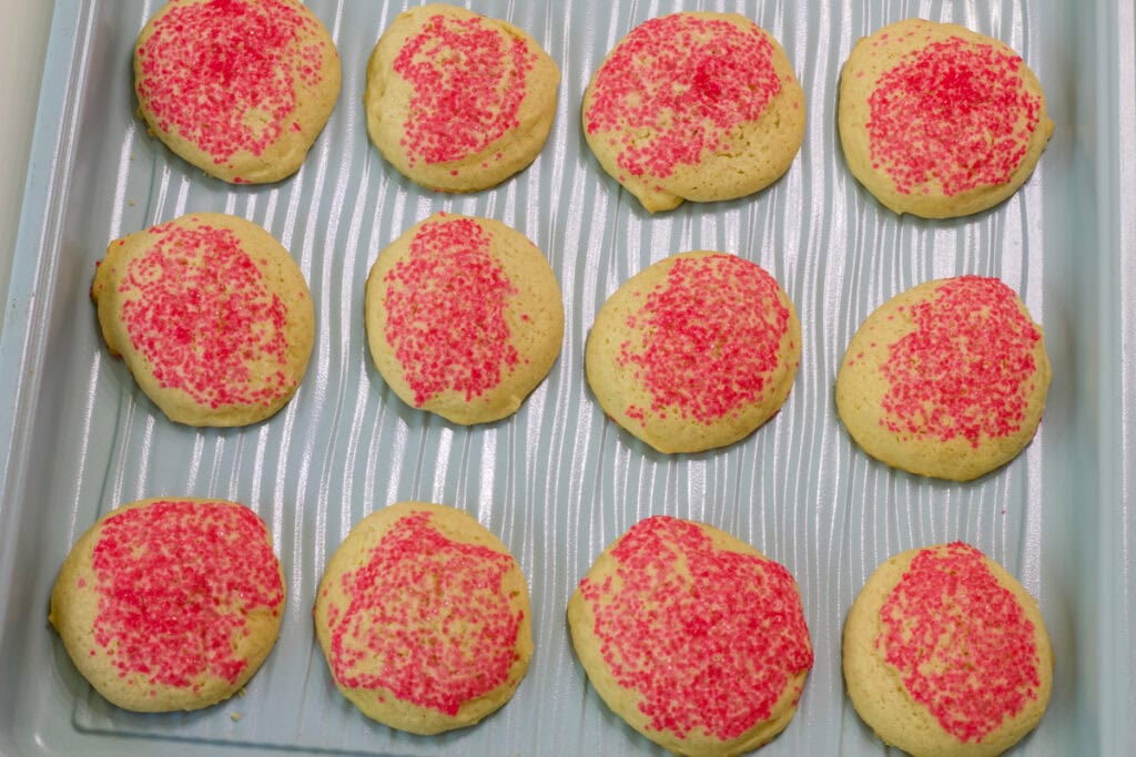 A dozen baked No Roll Sugar Cookies on a turquoise colored baking sheet.