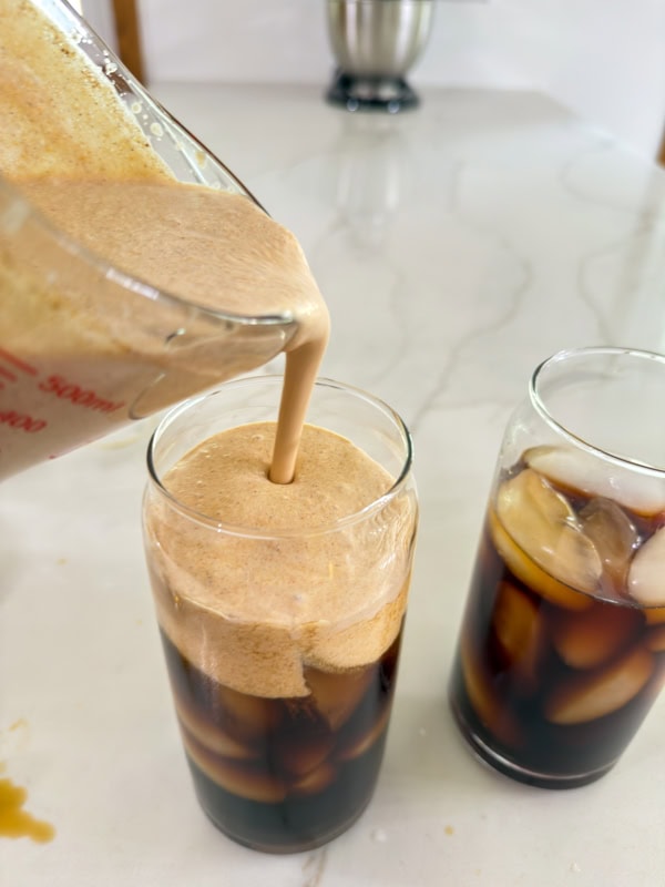 The creamy pumpkin foam being poured into the glass with the cold coffee.
