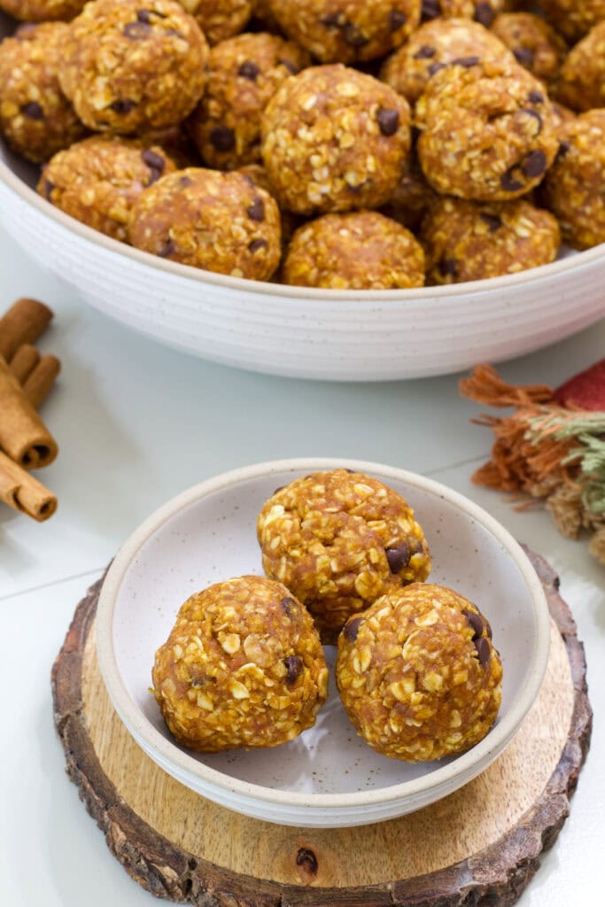 A small bowl of three Pumpkin Energy Balls in the foreground and a large bowl full in the background.