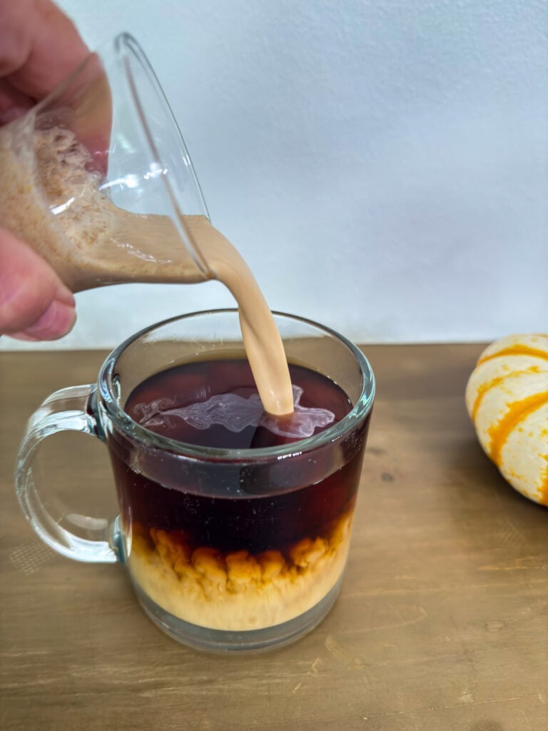 Some Pumpkin Spice Creamer being poured into a cup of hot coffee.