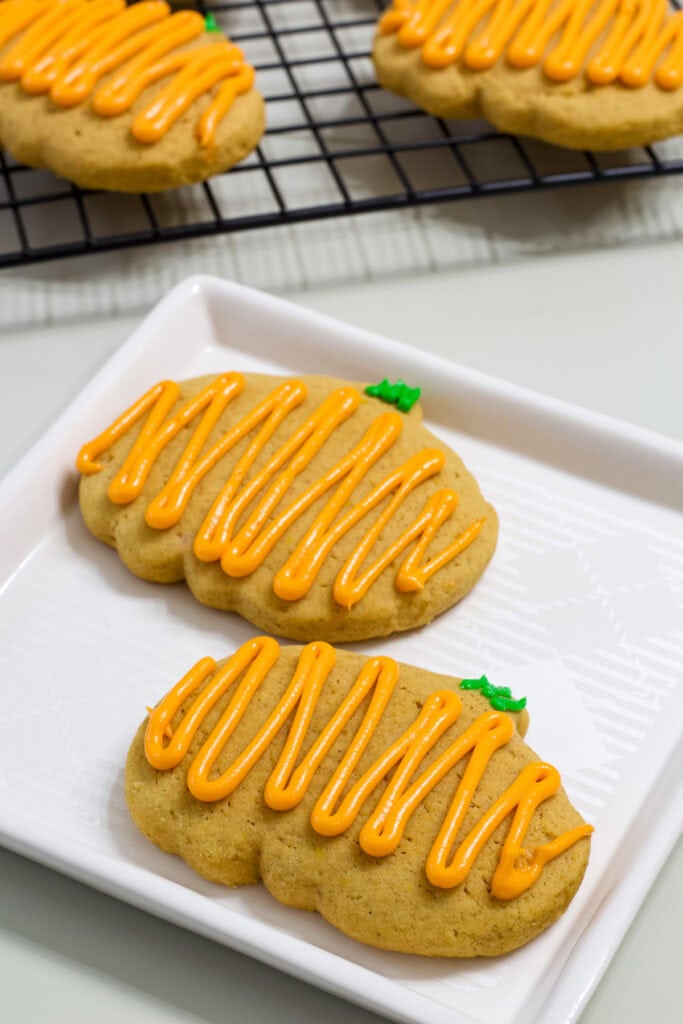 Two Pumpkin Spice Cutout Cookies on a plate in the foreground and several on a wire rack in the background.