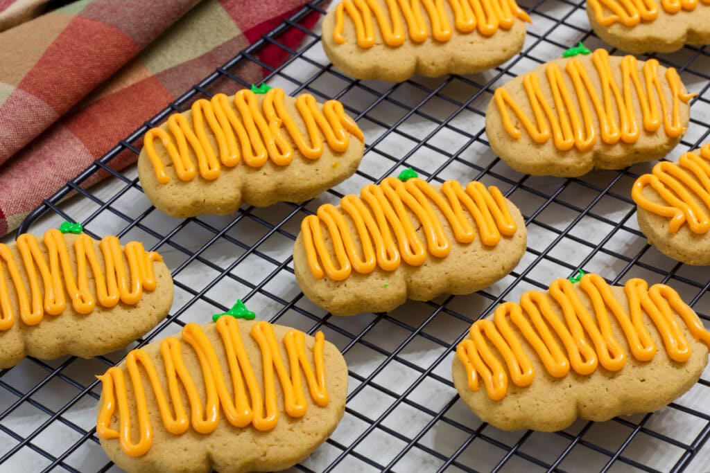 Several frosted Pumpkin Spice Cutout Cookies on a black wire cooling rack.