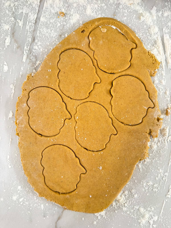 The cookie dough rolled out and pumpkin shapes are cut into it.