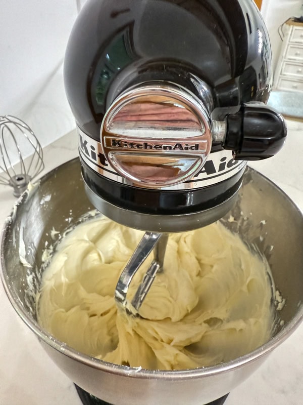 The ingredients for the cream cheese frosting mixed together in the bowl of a stand mixer.