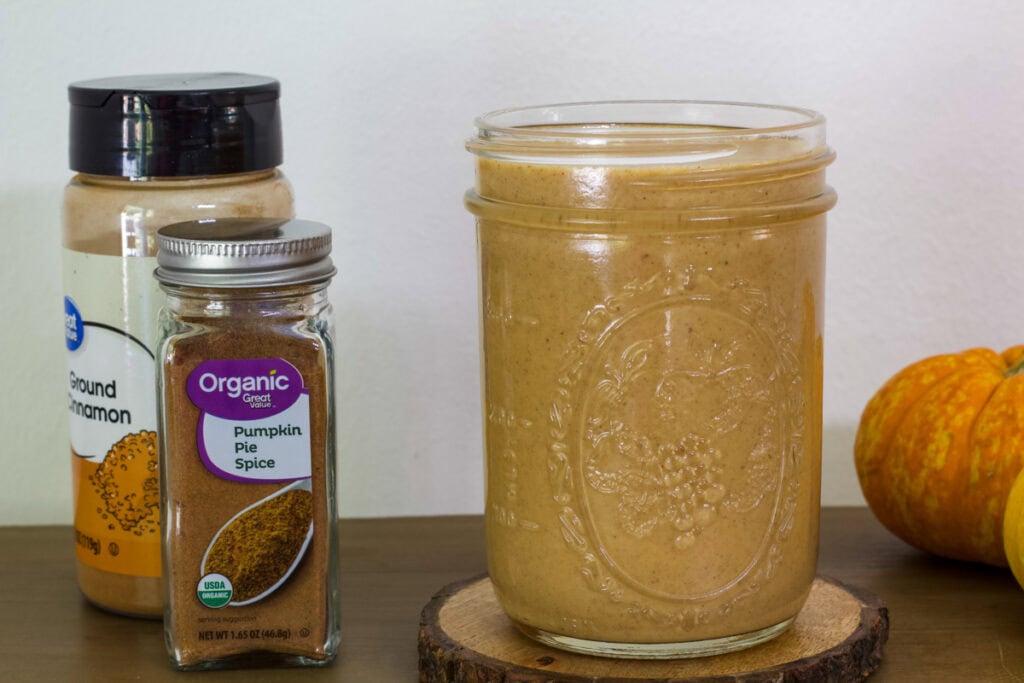 Side view of the jar full of pumpkin sauce and a bottle of cinnamon and pumpkin pie spice next to it.
