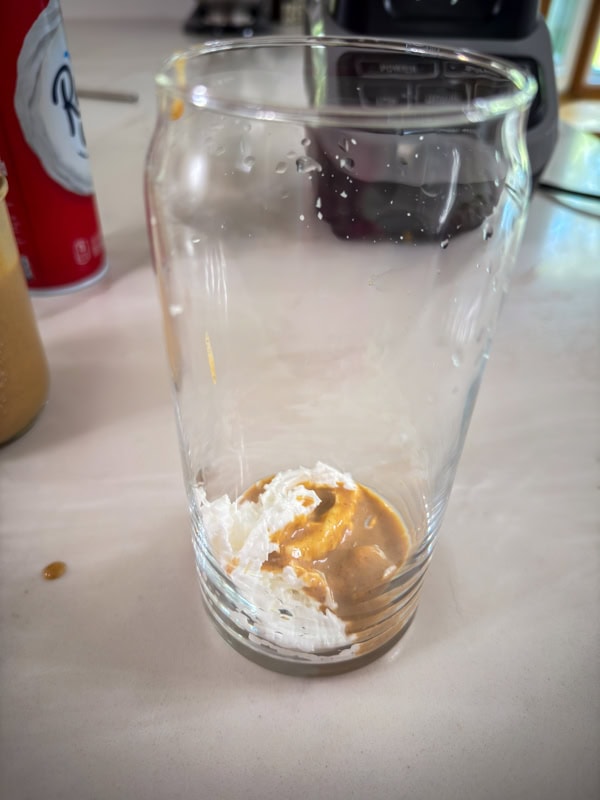 Some whipped cream and pumpkin sauce in the bottom of a glass.