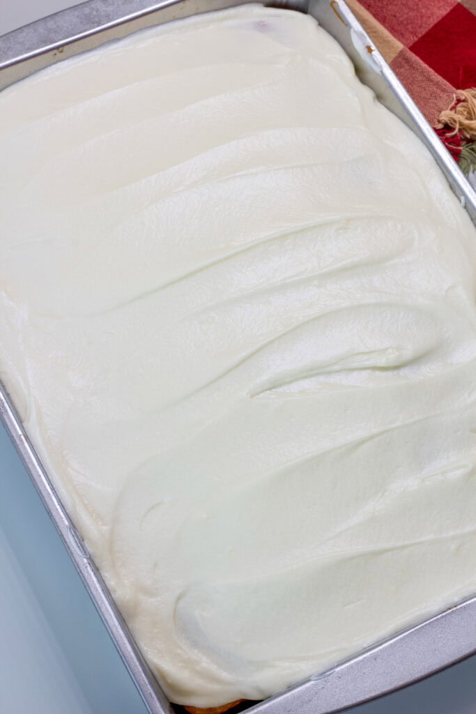 The entire uncut frosted Apple Cider Cake in a metal cake pan.
