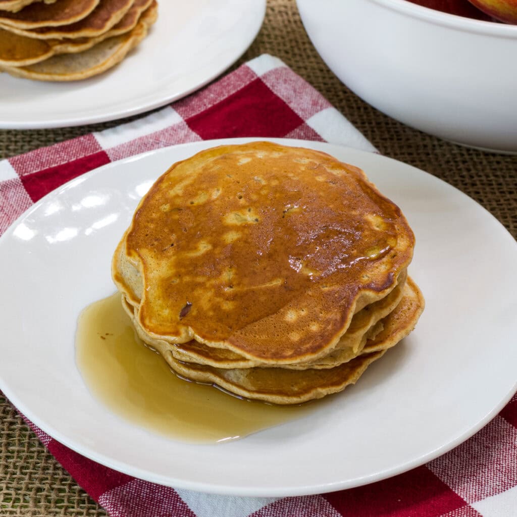 A stack of four Apple and Cinnamon Pancakes covered with syrup on a white plate.