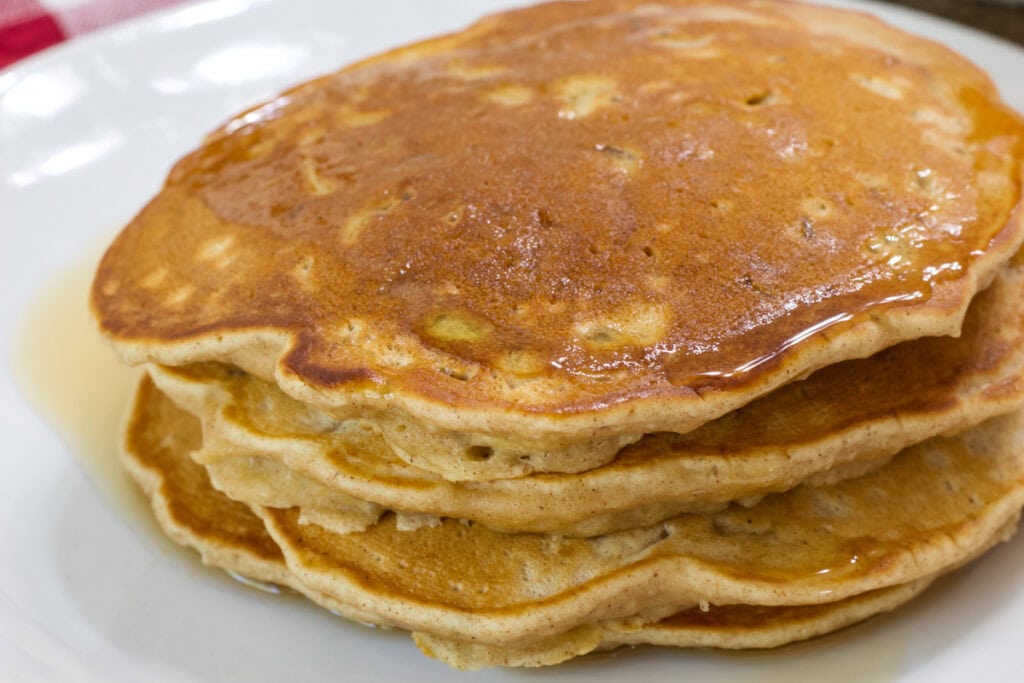 Close up side view of a stack of pancakes on a white plate.