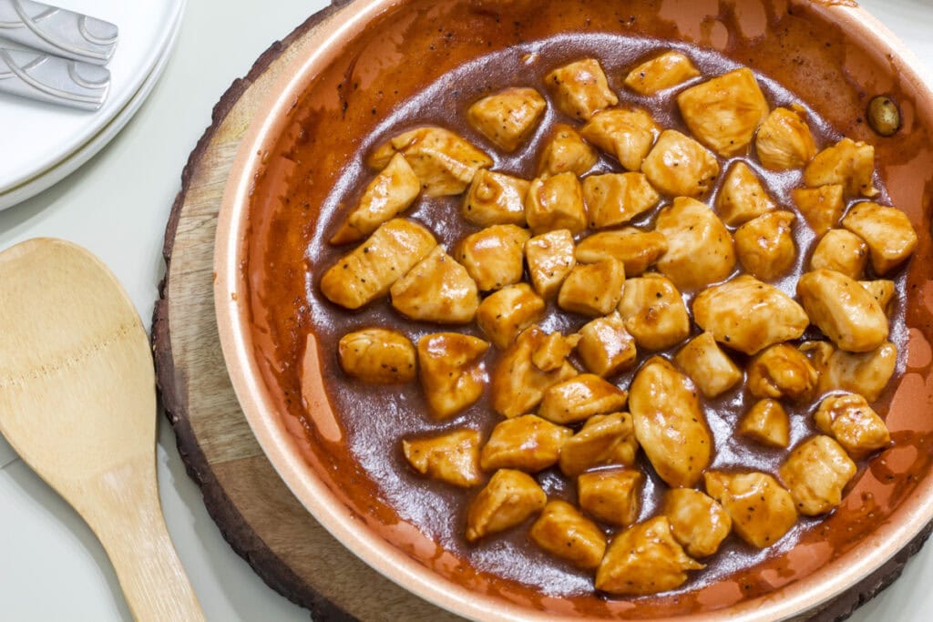A skillet full of the finished BBQ Chicken Bites with a wooden spoon next to it.