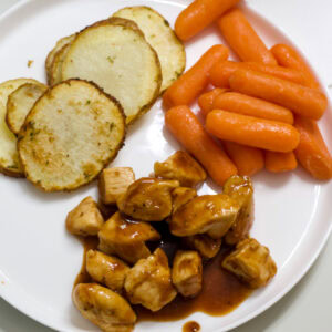Feature image of the chicken, air fried sliced potatoes and honey glazed carrots on a white plate.