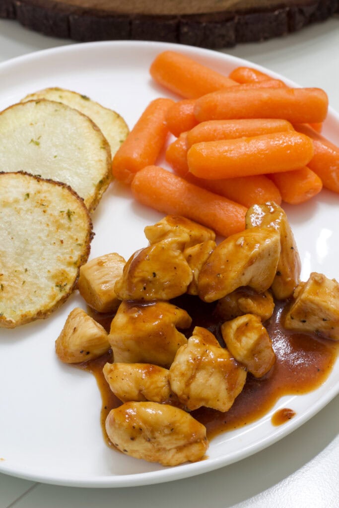 A plate with a serving of BBQ Chicken Bites and sliced potatoes and carrots.