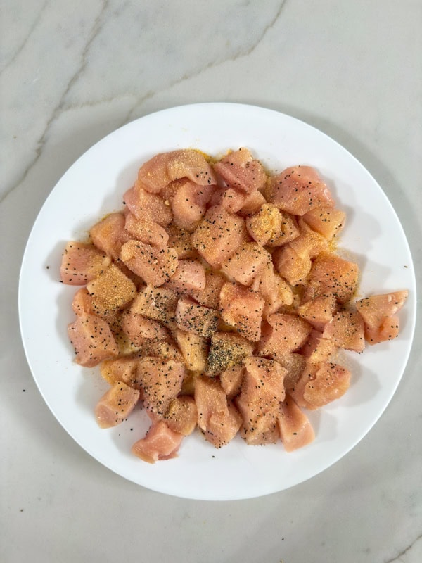 The raw, seasoned chicken pieces on a white plate ready to be cooked.