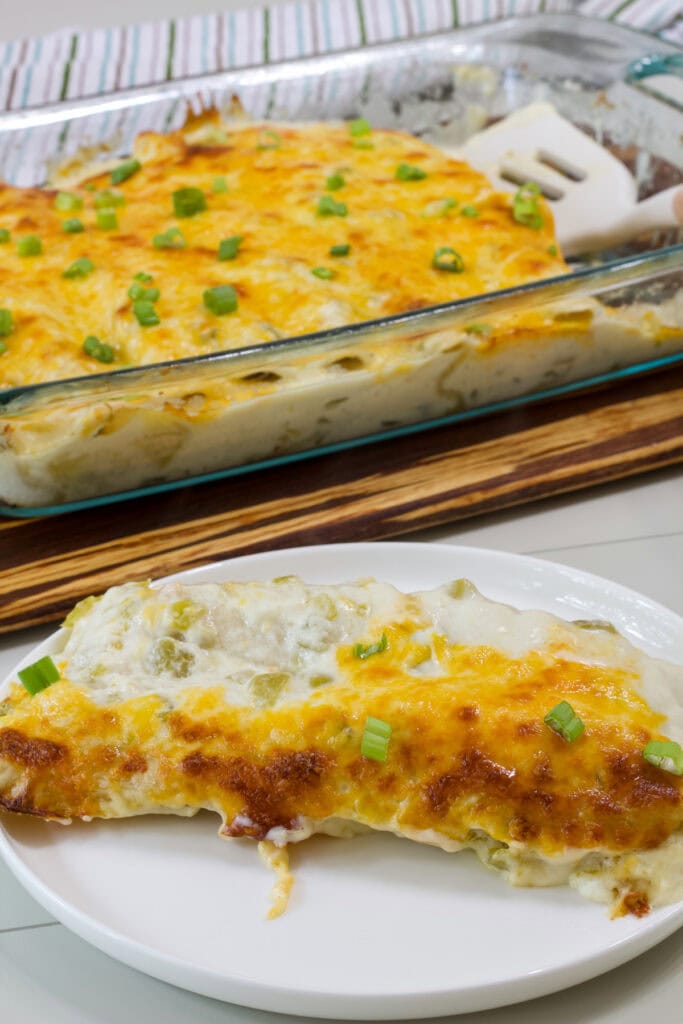 A white plate with two enchiladas on it in the foreground and the rest in the background.
