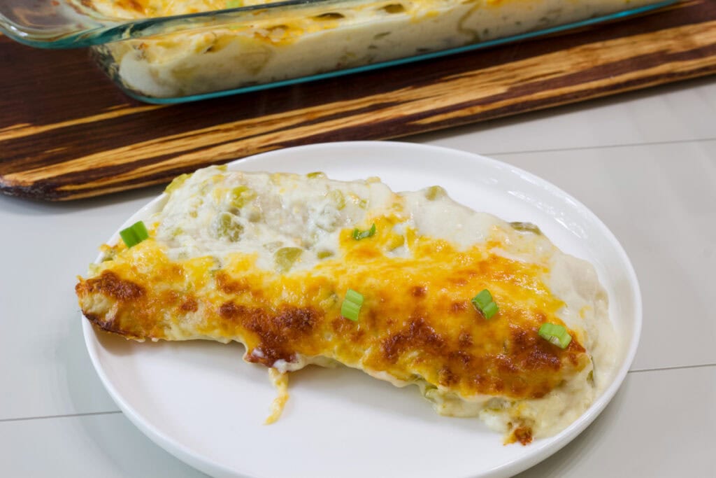 Close up of two Chicken Enchiladas with White Sauce on a white plate.
