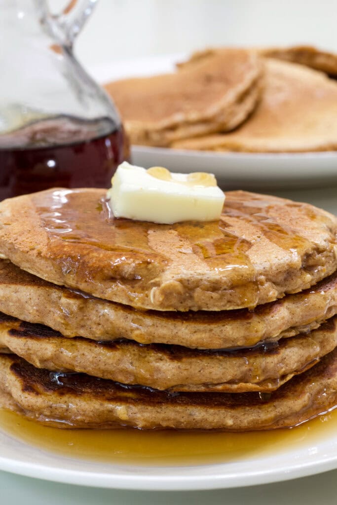 A stack of four Healthy Sweet Potato Pancakes topped with butter and syrup.