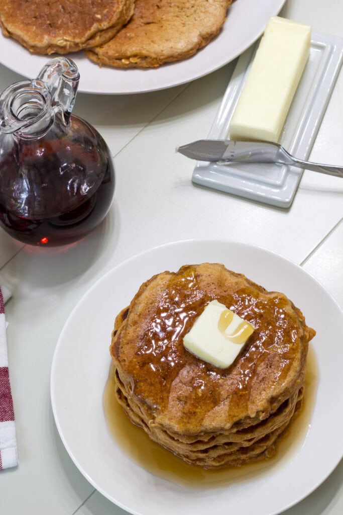 Overhead shot of a stack of pancakes, stick of butter, and bottle of syrup.