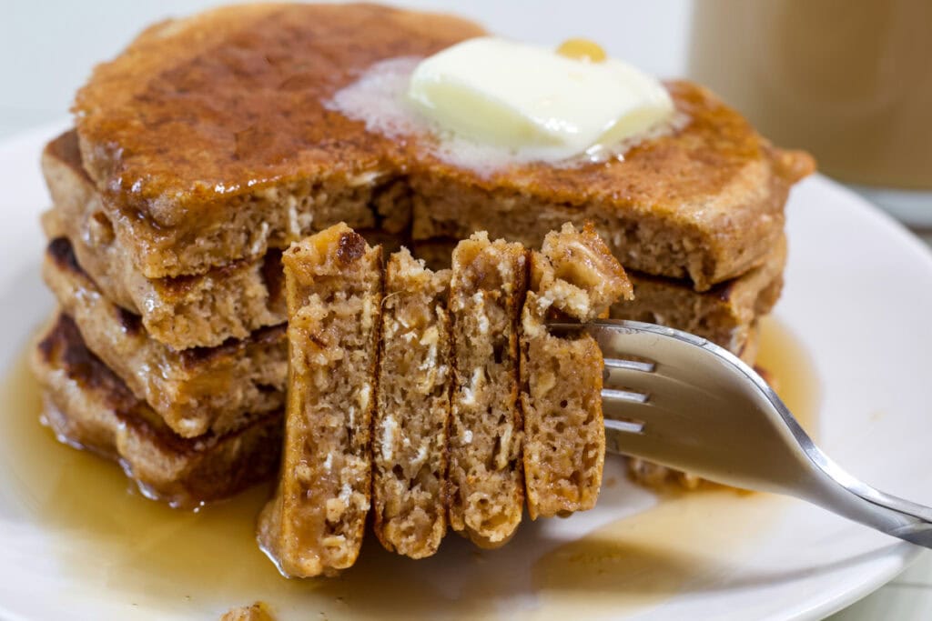 A bite of the stack of pancakes on a fork in front of the Healthy Sweet Potato Pancakes.