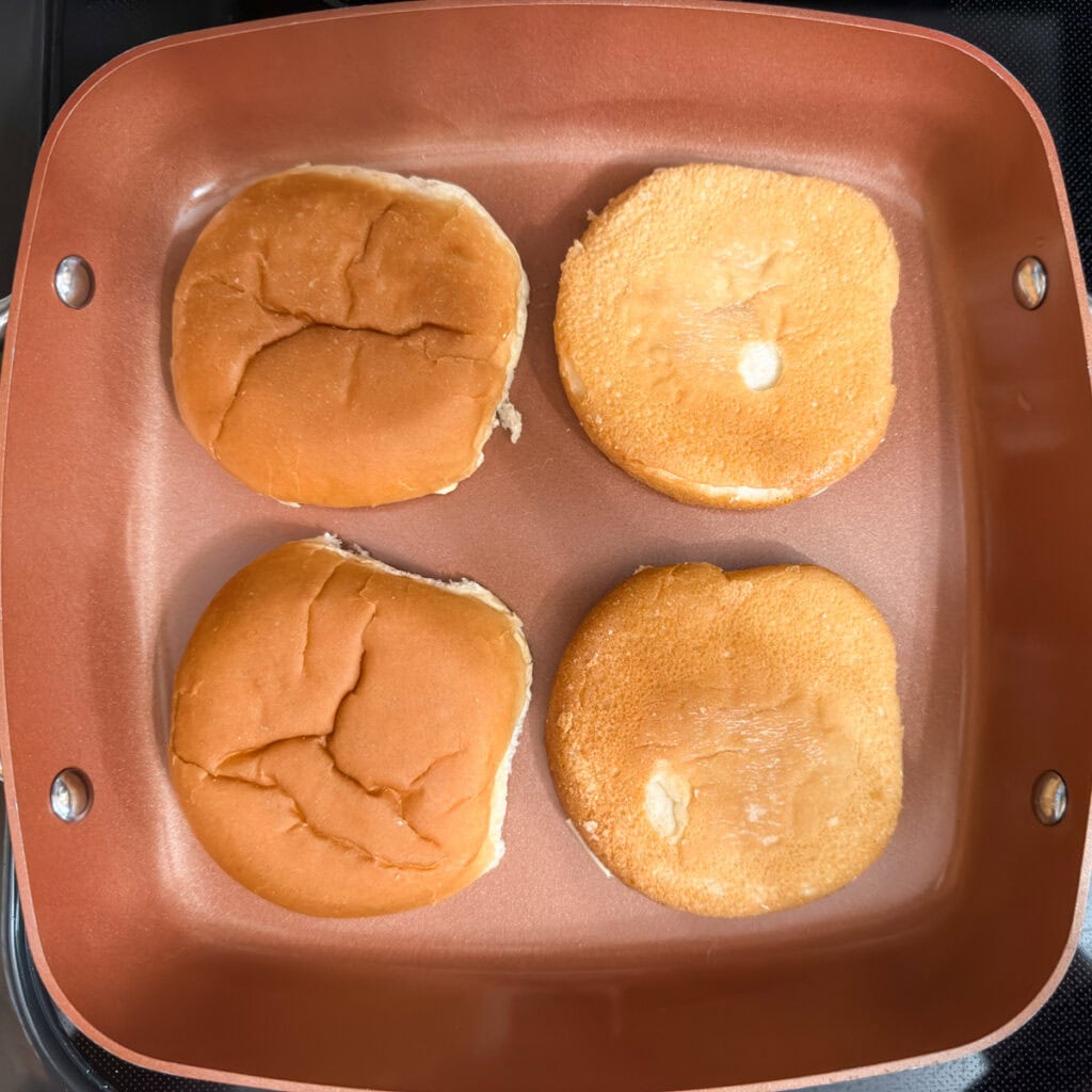 The buttered buns being toasted in a skillet.