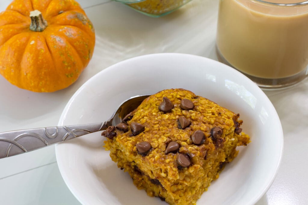 One serving of Pumpkin Chocolate Chip Baked Oatmeal in a bowl with a cup of coffee next to it.