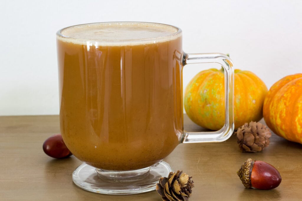Side view of one cup of Pumpkin Spice Latte with Oat Milk with some small pumpkins, acorns and small pinecones.