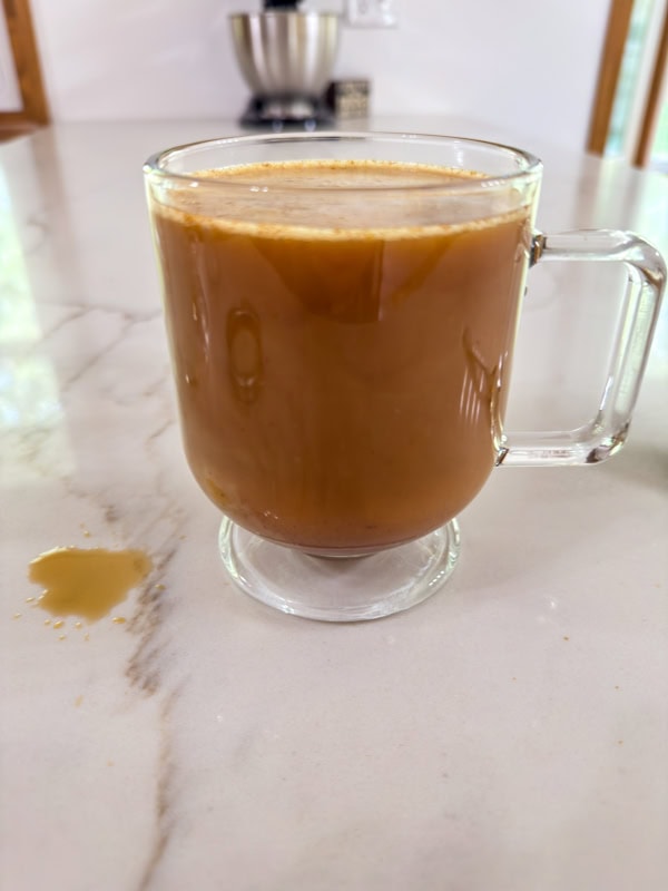 The oat milk has been added to the mug of pumpkin spice coffee.