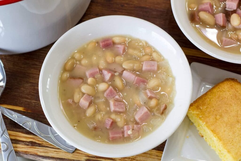 A bowl of 30-Minute White Beans with Ham and a piece of cornbread next to it.